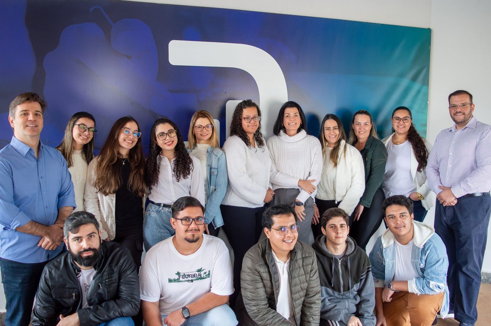 Equipe completa da ContDeal reunida em frente ao painel com a marca do escritório